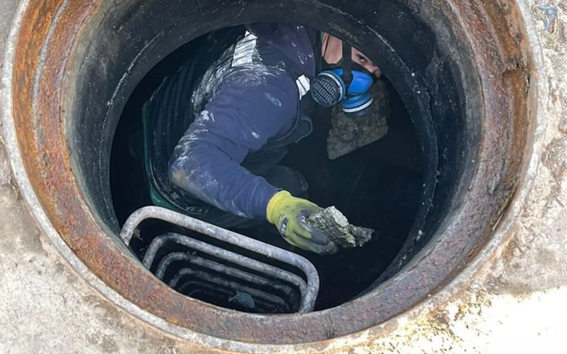 Trabajador con respirador realizando limpieza manual dentro de una cámara de inspección